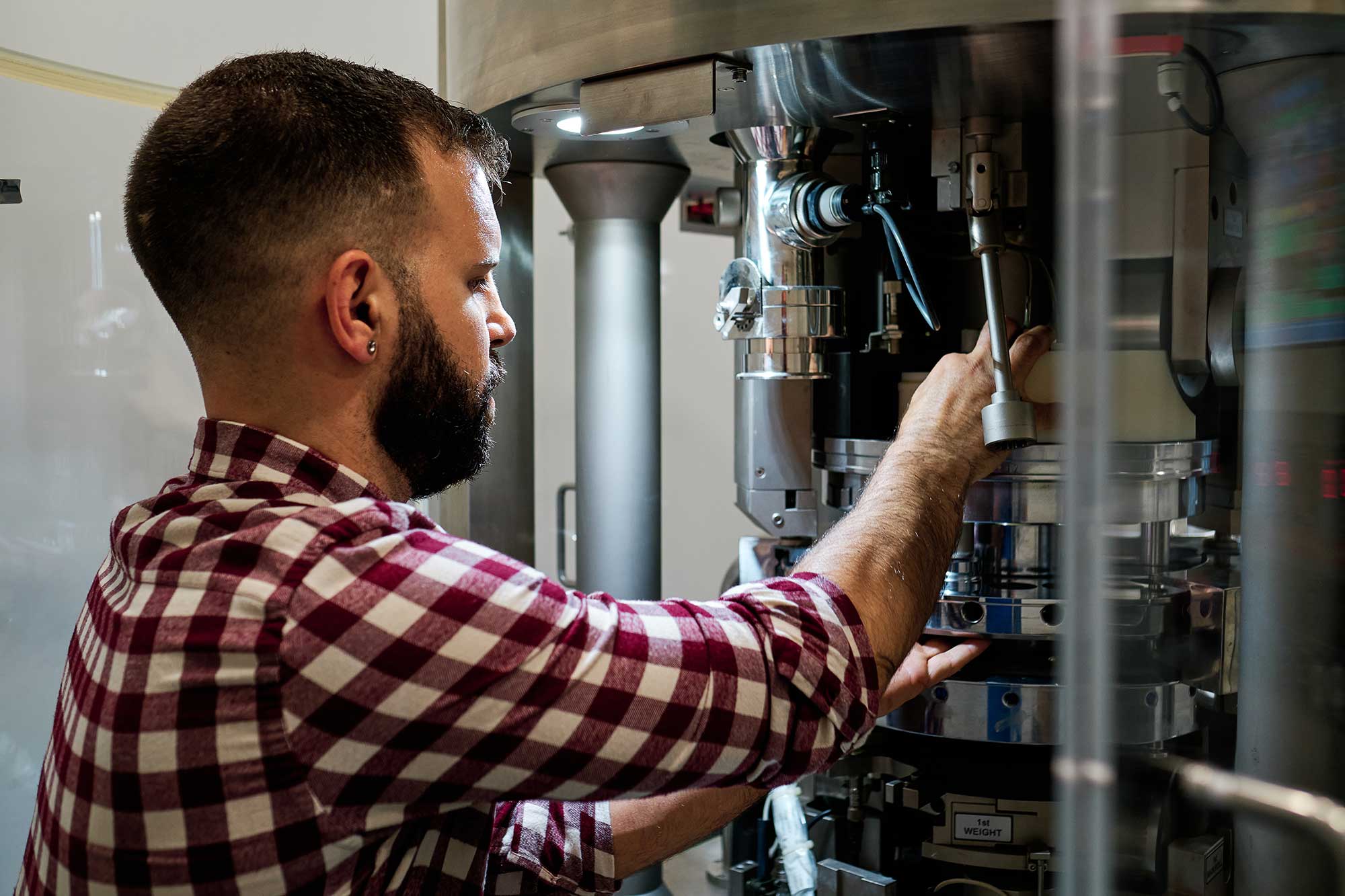 A technician in a checked shirt repairs a heating system, focusing on its internal components. Tools are visible as he works to ensure the system functions properly.